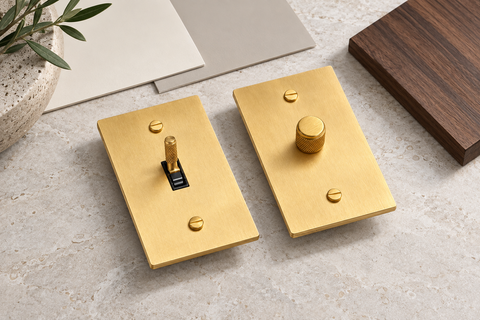 Satin brass toggle switch and rotary dimmer shown with paint and walnut samples for a renovation comparison.